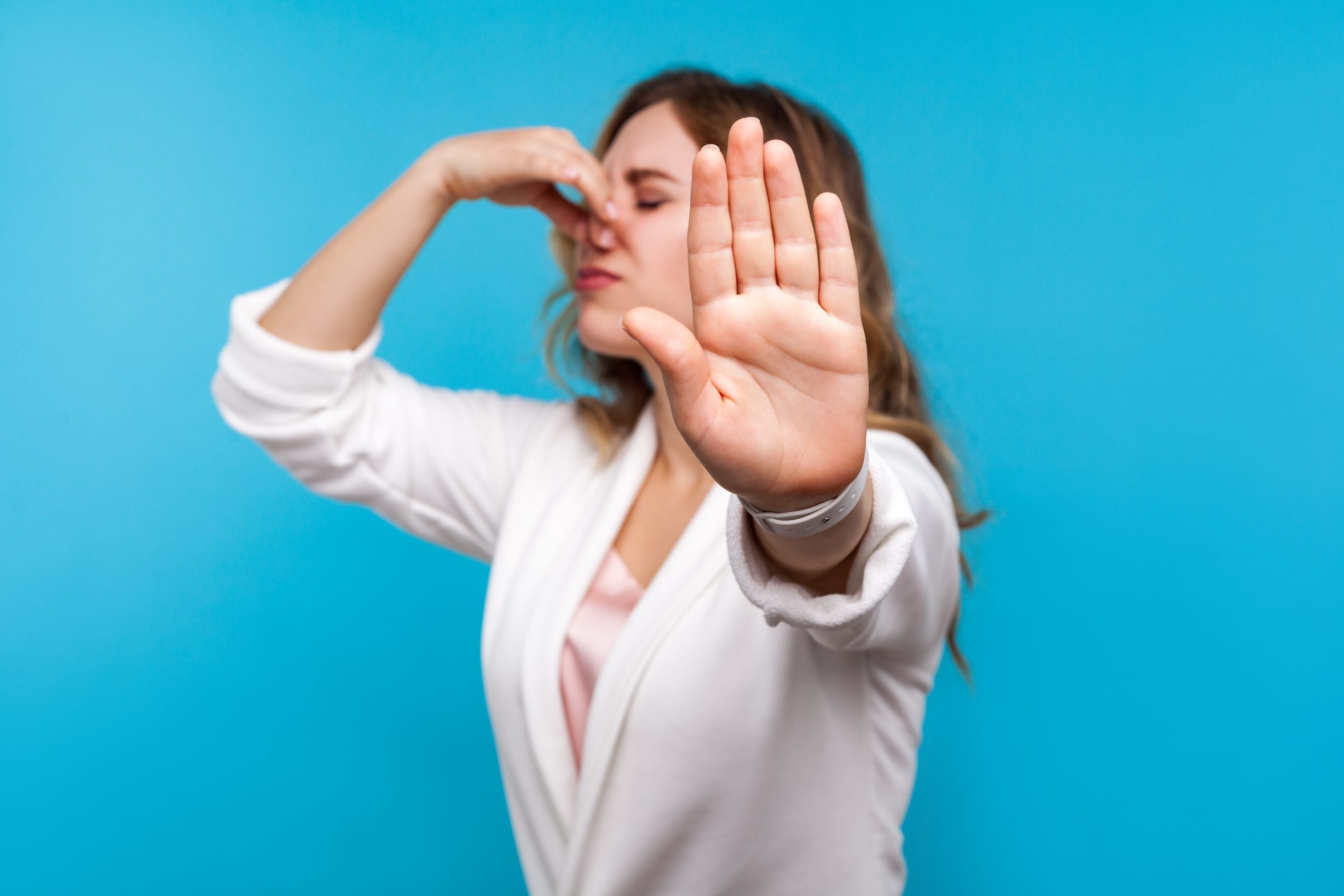 A woman holding her nose and holding her hand up to the camera in a "stop" signal.