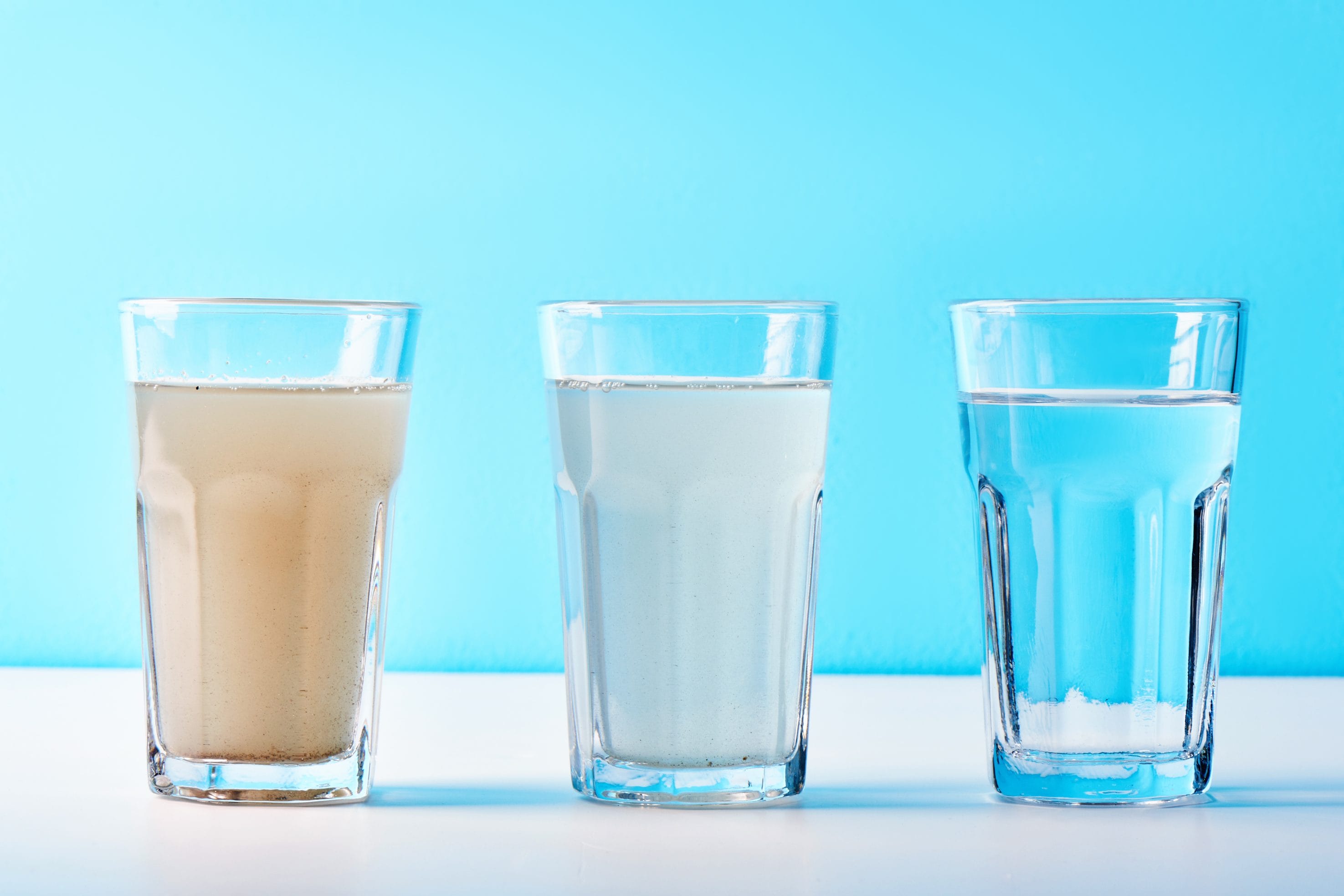 Three glasses of water against a blue background, varying from quite dirty on the left, a little cloudy in the middle, and crystal clear on the right.