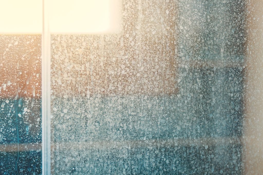 Adobe Stock image of a shower door that has hard water stains.