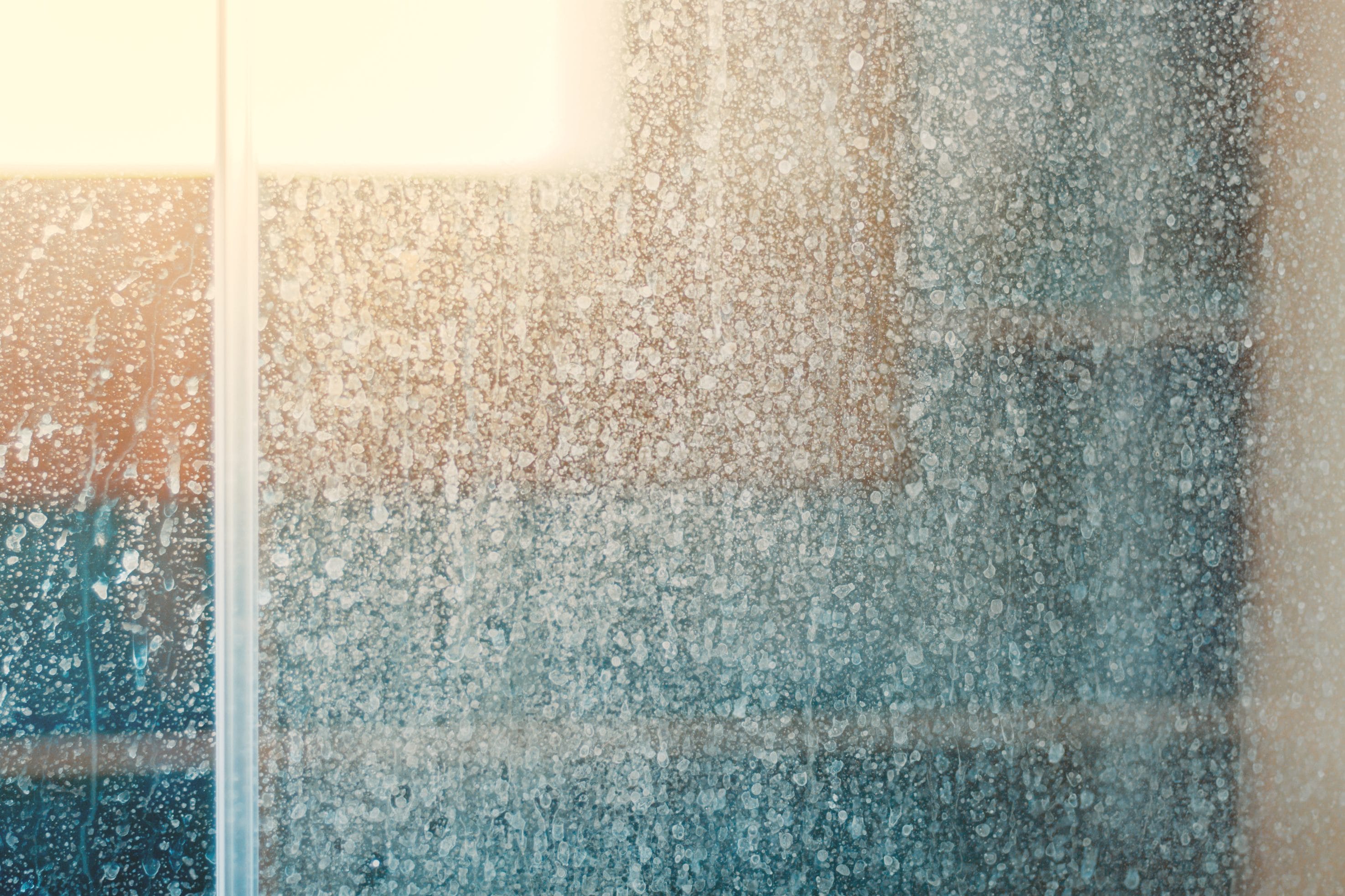 Adobe Stock image of a shower door that has hard water stains.